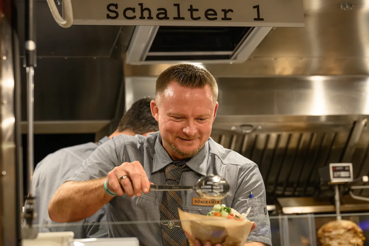 Mitarbeiter belegt an Schalter 1 des Foodtrucks einen frischen Döner im Fladenbrot